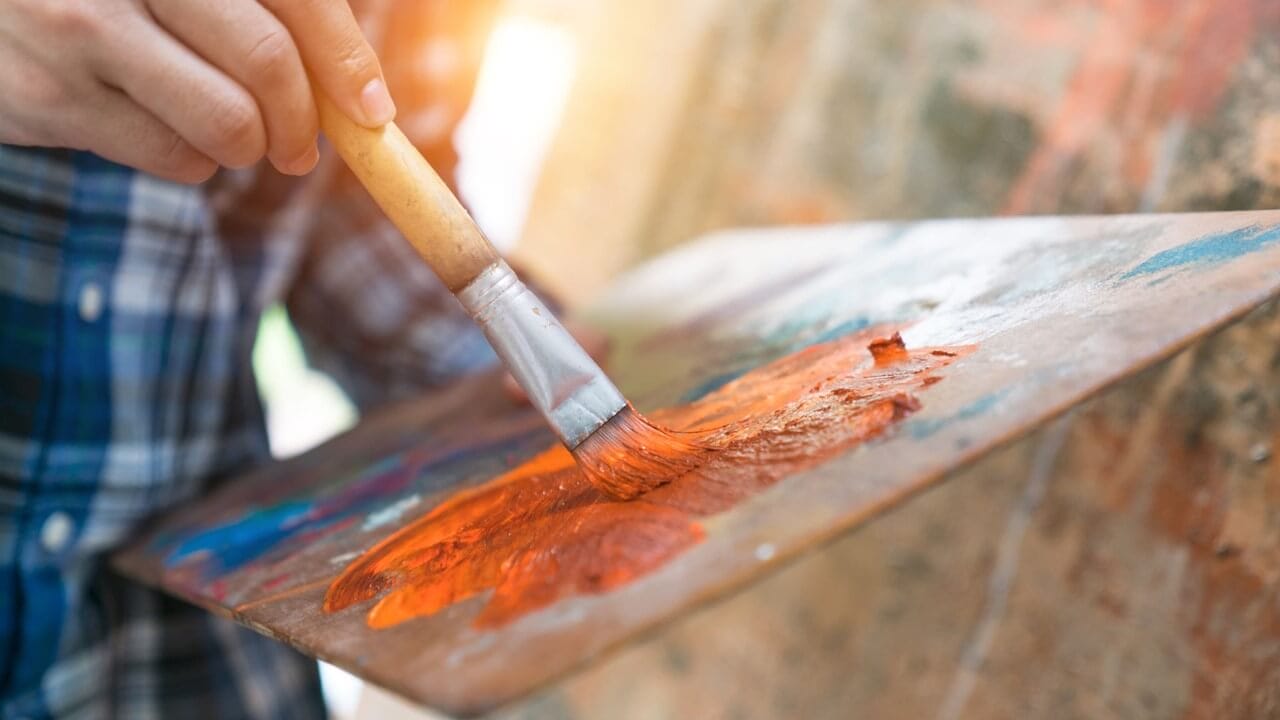 Persona con pincel en mano y una paleta de colores, creando una pintura a medida